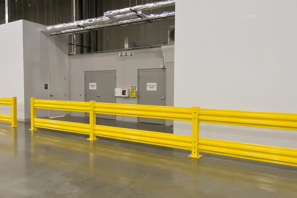 Bright yellow safety guardrails in an industrial facility positioned in front of gray utility doors and equipment.