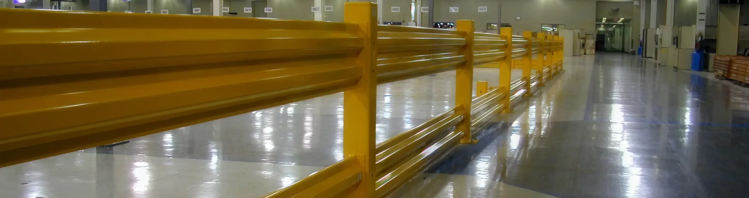 Long yellow steel safety barrier installed along the polished floor of an industrial facility.